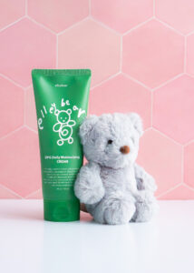 DPG Daily Moisturizing Cream - 200g Green tube ona pink tile background with a grey teddy bear