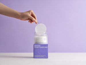 Behydy Plum Toner Pads, 150mL, housed in a clear, elegant container with a secure lid. The packaging highlights the plum-based formula, designed to gently exfoliate and hydrate the skin. Ideal for convenient, mess-free skincare routines.