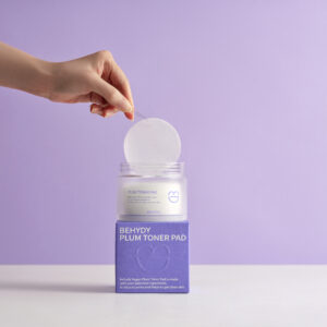 Behydy Plum Toner Pads, 150mL, housed in a clear, elegant container with a secure lid. The packaging highlights the plum-based formula, designed to gently exfoliate and hydrate the skin. Ideal for convenient, mess-free skincare routines.